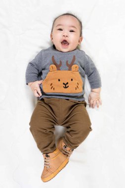 Hoş 4 ay, şık kıyafetler içinde küçük Asyalı erkek bebek ve yumuşak battaniyenin üzerine uzanmış bebek botları evde mutlu bir şekilde gülümsüyor.