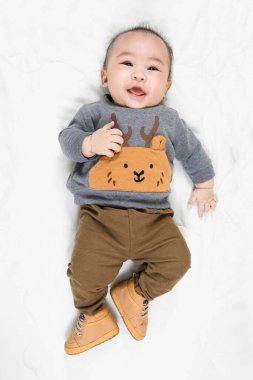 Hoş 4 ay, şık kıyafetler içinde küçük Asyalı erkek bebek ve yumuşak battaniyenin üzerine uzanmış bebek botları evde mutlu bir şekilde gülümsüyor.