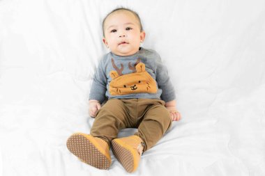 4 aylık şirin Asyalı erkek bebek şık kıyafetler içinde ve bebek botları beyaz battaniyede oturmuş evde mutlu bir şekilde çocuk modasında..