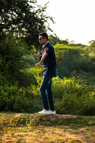 Mavi gömlek ve kot pantolon giyen Hintli genç bir adamın portresi.