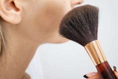 Kız elinde bir makyaj fırçası tutuyor ve makyaj yapıyor.