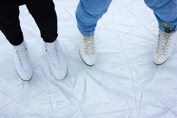 Primo piano di pattinaggio su ghiaccio femminile piedi in inverno su una pista di pattinaggio all'aperto. Pattini su ghiaccio di due amici che pattinano insieme in una giornata invernale. Orario invernale, attività all'aria aperta, concetto di svago invernale — Foto Stock