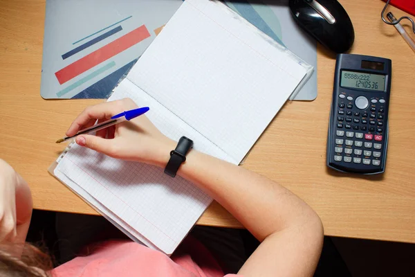 Kız oturma odasında matematik ödevi yapıyor. Masasında Otururken Ders Kitaplarında Kalem Yazıyor ve Bilgisayarını Kullanıyor. İnternetten Öğreniyor
