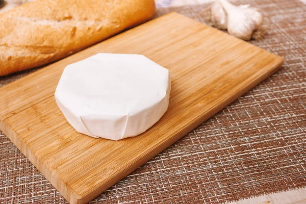 Queijo mofado em uma embalagem de papel. camembert em embalagem de papel branco na mesa da cozinha — Fotografia de Stock