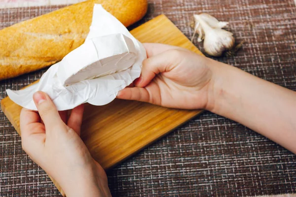 Руки распаковка camembert cheese.camembert в упаковке из белой бумаги. сыр с белым плесневым сыром — стоковое фото