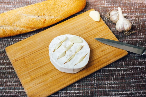 DIY queso horneado camembert instrucción paso a paso. paso 2 hacer cortes en el camembert e insertar el ajo en los cortos.queso con queso moldeado blanco — Foto de Stock