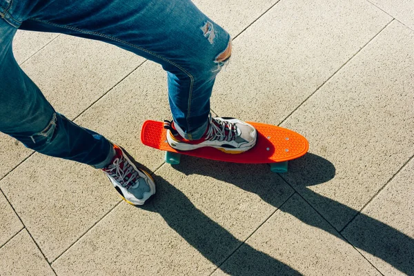 Un joven con vaqueros rasgados de pie con una tabla de peniques en el parque. actividades de verano skateboarding — Foto de Stock