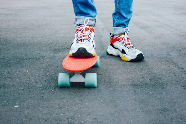 Un joven con vaqueros rasgados de pie con una tabla de peniques en el parque. actividades de verano skateboarding —  Fotos de Stock