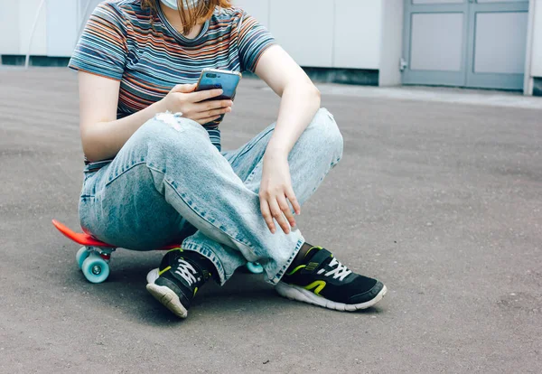 Summer lifestyle image of trendy pretty girl sitting on quay on the big city background. Smiling, texting a message, enjoying sun. — Stock Photo, Image