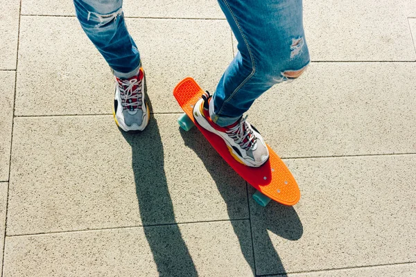 Un joven con vaqueros rasgados de pie con una tabla de peniques en el parque. actividades de verano skateboarding — Foto de Stock