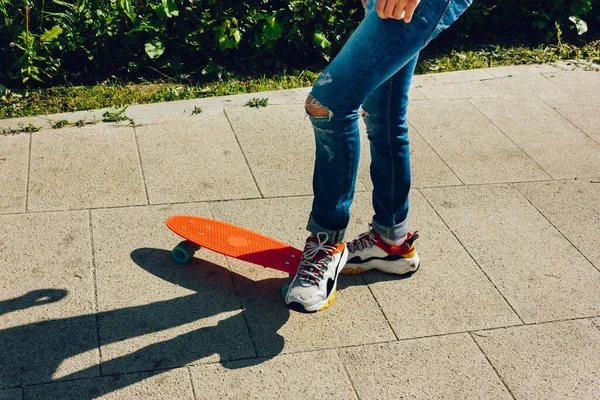 Молодий хлопець у рваних джинсах стоїть з дошкою пенні в парку. літні заходи скейтбординг — стокове фото