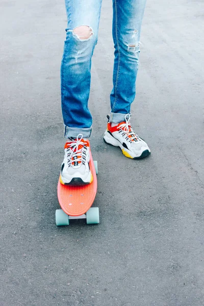 Un joven con vaqueros rasgados de pie con una tabla de peniques en el parque. actividades de verano skateboarding — Foto de Stock