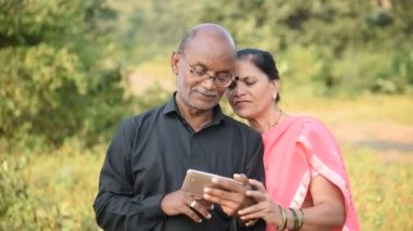 Mutlu Hintli çift akıllı telefon kullanıyor, akıllı telefondan fotoğraflara bakıyor, dışarıda birlikte gülüyor ve gülümsüyorlar..