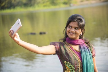 Mutlu genç Hintli kız dışarıda akıllı telefondan selfie çekiyor.. 