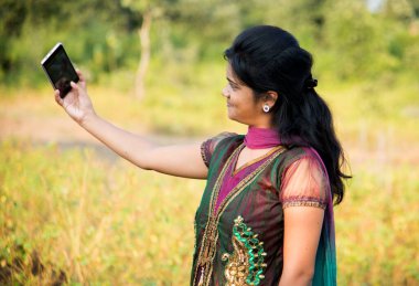 Mutlu genç Hintli kız dışarıda akıllı telefondan selfie çekiyor.. 