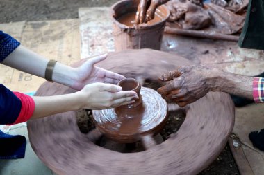 Bir çömlekçinin elleri, tekerleğin üzerinde toprak kavanozu yaratıyor. Kadın ellerine rehberlik eden bir çömlekçi 