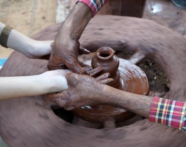 Bir çömlekçinin elleri, tekerleğin üzerinde toprak kavanozu yaratıyor. Kadın ellerine rehberlik eden bir çömlekçi 