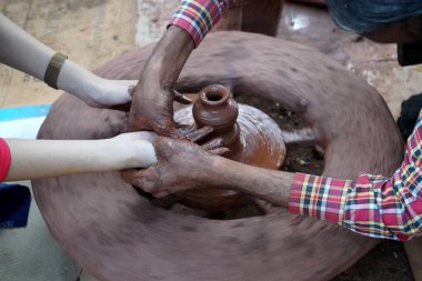 Bir çömlekçinin elleri, tekerleğin üzerinde toprak kavanozu yaratıyor. Kadın ellerine rehberlik eden bir çömlekçi 