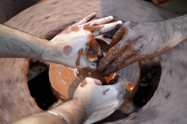 Bir çömlekçinin elleri, tekerleğin üzerinde toprak kavanozu yaratıyor. Kadın ellerine rehberlik eden bir çömlekçi 