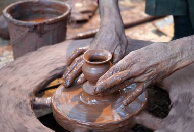 Bir çömlekçinin elleri, tekerleğin üzerinde toprak kavanozu yaratıyor. Kadın ellerine rehberlik eden bir çömlekçi 