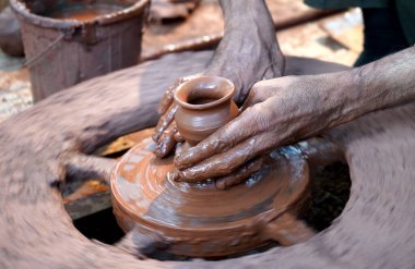 Bir çömlekçinin elleri, tekerleğin üzerinde toprak kavanozu yaratıyor. Kadın ellerine rehberlik eden bir çömlekçi 