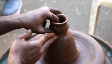 Bir çömlekçinin elleri, tekerleğin üzerinde toprak kavanozu yaratıyor. Kadın ellerine rehberlik eden bir çömlekçi 