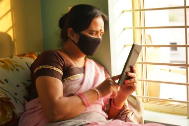 Yüz koruyucu maskeli Hintli kadın tabletten haber okuyor..