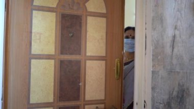 Karantinadaki kadın maske takıyor ve Coronavirüs salgını sırasında kapıyı açıyor, Coronavirus salgını ya da Covid-19.