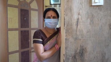 Karantinadaki kadın maske takıyor ve Coronavirüs salgını sırasında kapıyı açıyor, Coronavirus salgını ya da Covid-19.