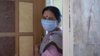 Karantinadaki kadın maske takıyor ve Coronavirüs salgını sırasında kapıyı açıyor, Coronavirus salgını ya da Covid-19.