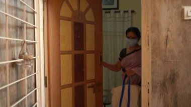 Karantinadaki kadın maske takıyor ve Coronavirüs salgını sırasında kapıyı açıyor, Coronavirus salgını ya da Covid-19.
