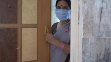 Karantinadaki kadın maske takıyor ve Coronavirüs salgını sırasında kapıyı açıyor, Coronavirus salgını ya da Covid-19.