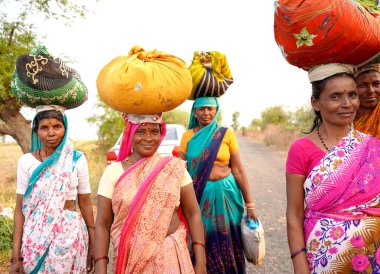  AMRAVATI, MAHARASHTRA, INDIA, 18 Mart 2020: Hindistan kırsal kesimindeki kadınlar işten eve giderken kafalarında tomar para taşıyorlar. 