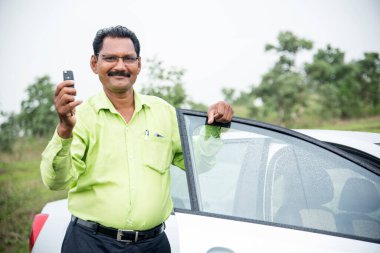 Mutlu genç Hintli adam yeni arabasının anahtarını tutuyor.