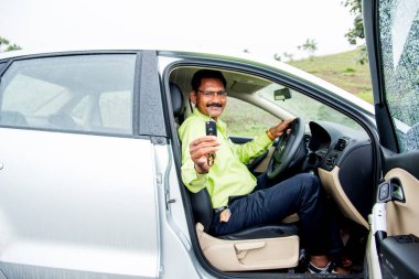 Mutlu genç Hintli adam yeni arabasının anahtarını tutuyor.