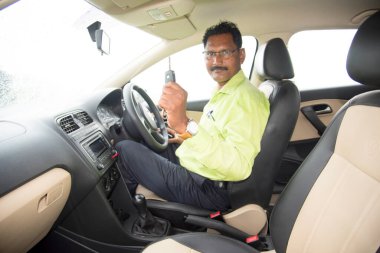 Mutlu genç Hintli adam yeni arabasının anahtarını tutuyor.