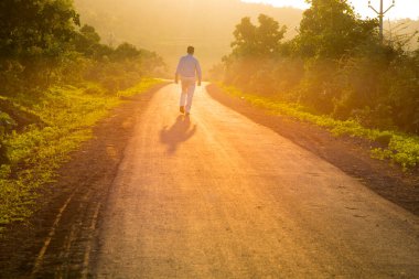 Genç adam gün doğumunda orman yolunda yürüyor.