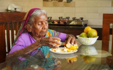 Yaşlı Hintli kadın kahvaltı masasında sağlıklı portakal yiyor..