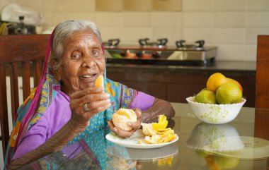 Yaşlı Hintli kadın kahvaltı masasında sağlıklı portakal yiyor..