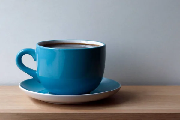 Blue coffee Cup with saucer on wooden table top in daylight
