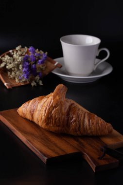 Siyah arka planda tahta kesme tahtasındaki kruvasan.