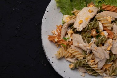 Makarna kızartılmış ve siyah arka planda seramik tabakta tavuk var.