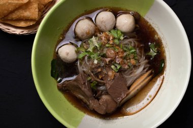 Siyah arka planda bir fincanda haşlanmış domuz etli erişte.