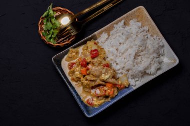 Kızarmış domuz köri tozu ile buharda pişmiş pirinci siyah arka planda bir tabakta karıştır.