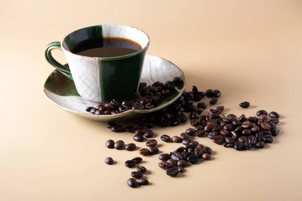 Hot black coffee in green coffee cup and coffee beans on a brown Klang background.