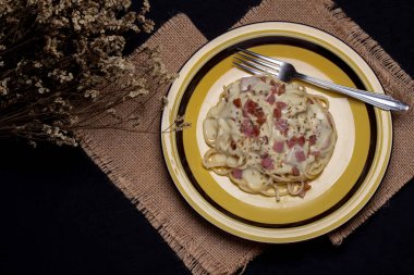 Jambonlu Carbonara spagettisi, siyah bir masada sarı bir tabakta kekik..