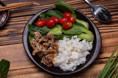 Teriyaki domuz eti üzerine susam ve sebze serpilmiş ve siyah tabakta pilav..