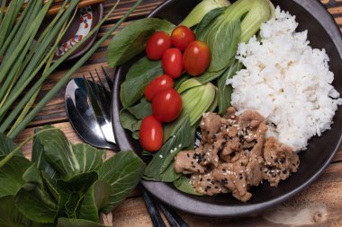 Teriyaki domuz eti üzerine susam ve sebze serpilmiş ve siyah tabakta pilav..