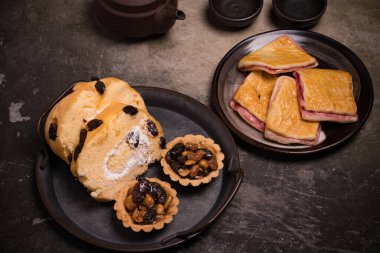 Antika tepside fırın, ekmek, reçel, rulo, meyveli tart. Koyu ton.