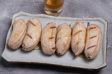 Gri bir arka planda, üzerinde bal bulunan ızgara muzlar..